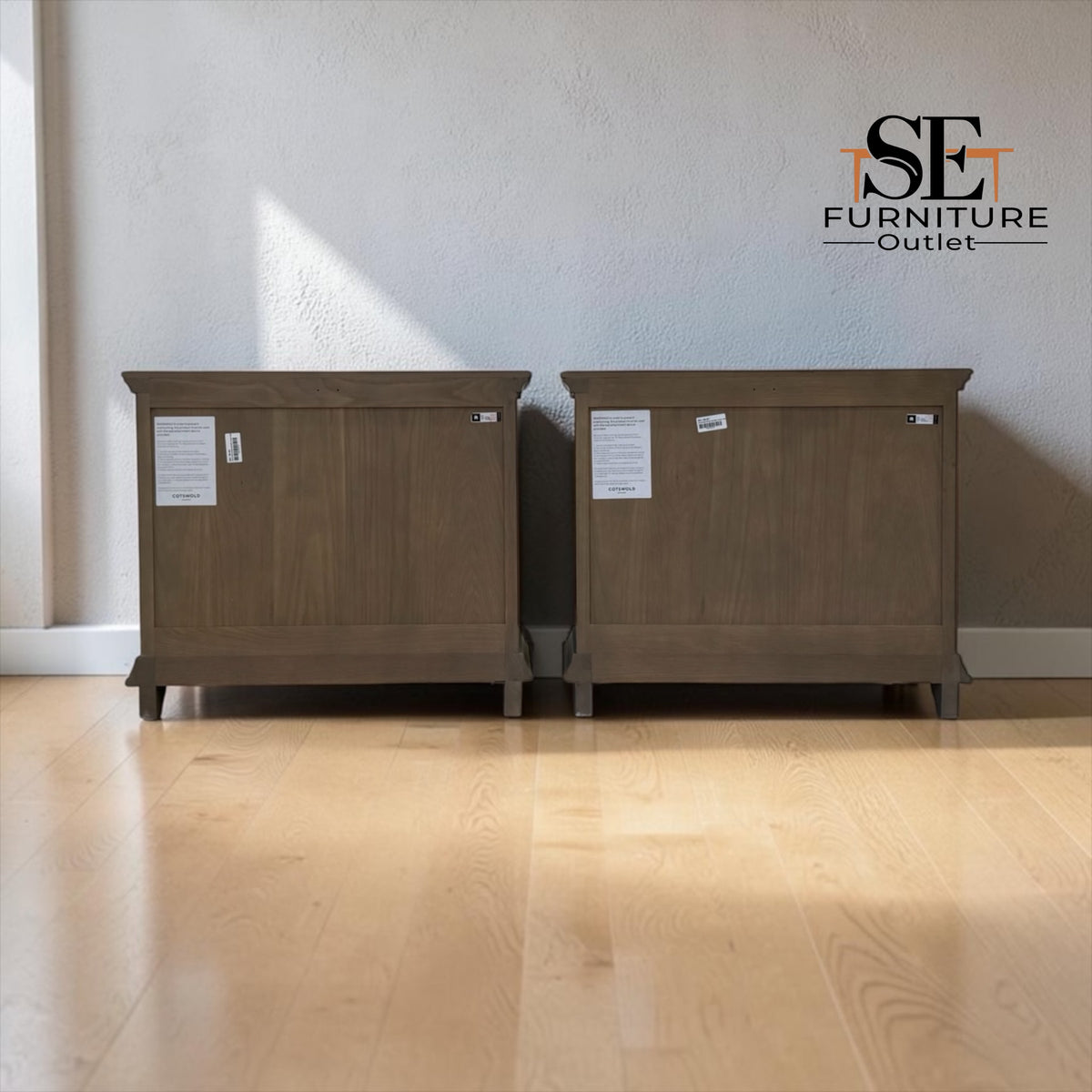 Two matching medium-brown wooden storage cabinets or side tables with white product tags, shown side-by-side on a light wood floor against a textured off-white wall. An 'SE FURNITURE Outlet' logo is visible in the top right corner.