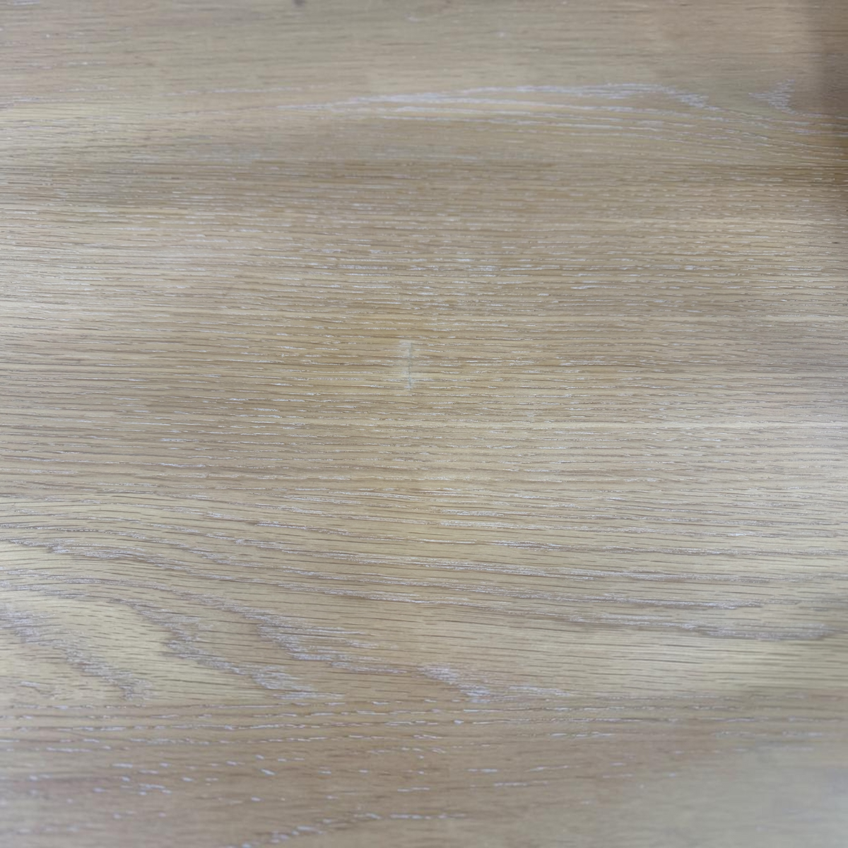 A close-up view of a light oak wood grain surface, showing natural texture and subtle variations in tone.