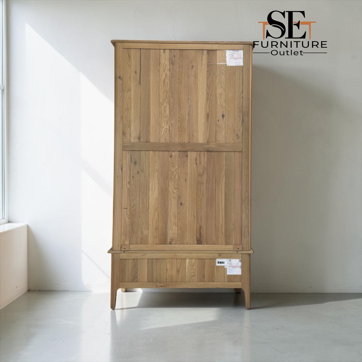 A tall wooden storage cabinet with two upper doors and a lower drawer, shown in a minimalist room with a white wall and gray floor. The cabinet has a natural oak finish with visible wood grain.

