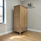 A tall two-door wooden wardrobe in a natural oak finish, positioned in a room corner with light gray walls and a wood floor. The brand logo 'SE FURNITURE Outlet' is visible in the top right corner.

