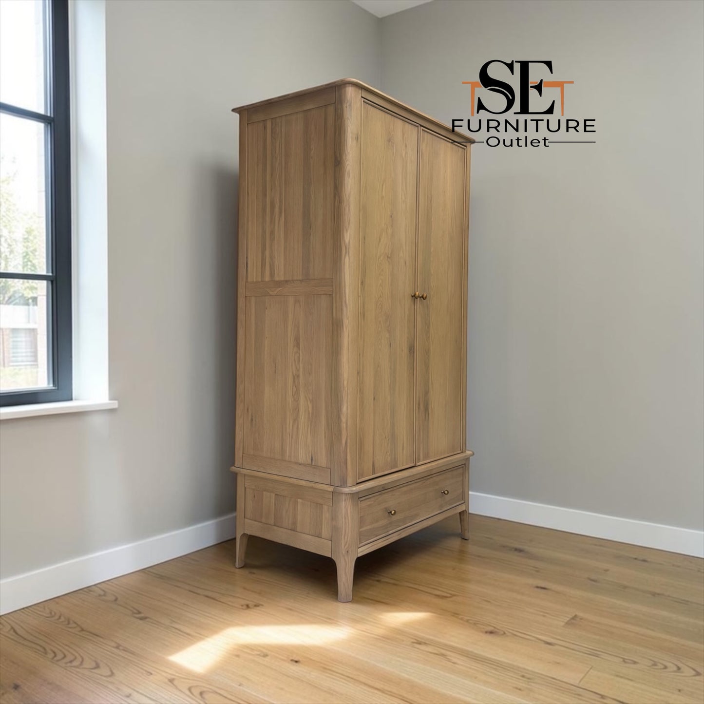 A tall two-door wooden wardrobe in a natural oak finish, positioned in a room corner with light gray walls and a wood floor. The brand logo 'SE FURNITURE Outlet' is visible in the top right corner.


