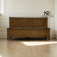 A wooden storage bench with a slatted backrest and turned legs, shown in a bright room with light wood flooring and white shiplap walls. The SE Furniture Outlet logo is visible in the upper right.

