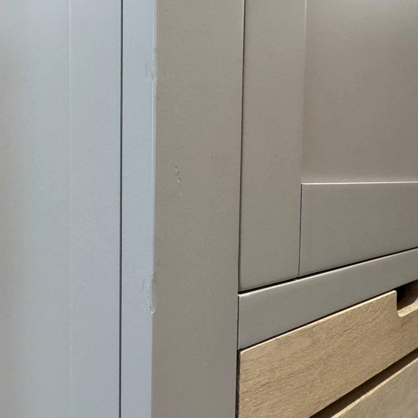 Close-up of a light gray cabinet or drawer unit with a wood-grain drawer front visible at the bottom right.

