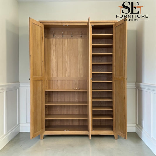 A tall wooden three-door wardrobe or closet with two doors open, showing a hanging rod, interior shelves, and multiple adjustable shelves. The cabinet is photographed in a real room with white walls and wainscoting, and the SE Furniture Outlet logo appears in the top right corner.

