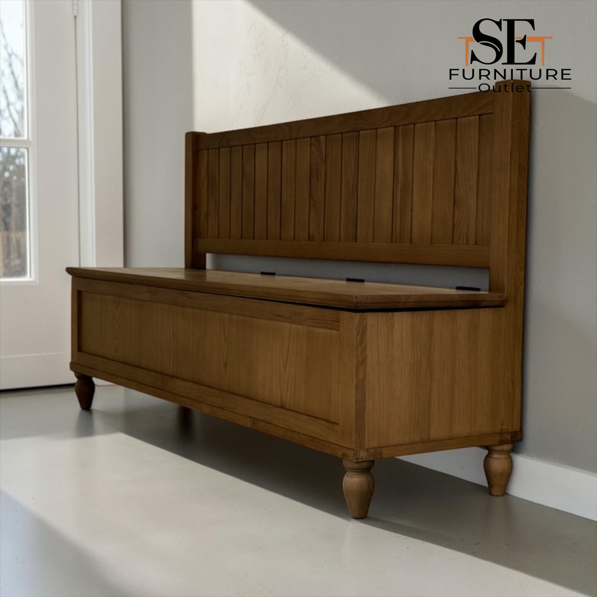 A wooden storage bench with a tall slatted backrest and turned legs, shown in a bright room with a white door and gray floor. The SE Furniture On brand logo is visible in the top right corner.

