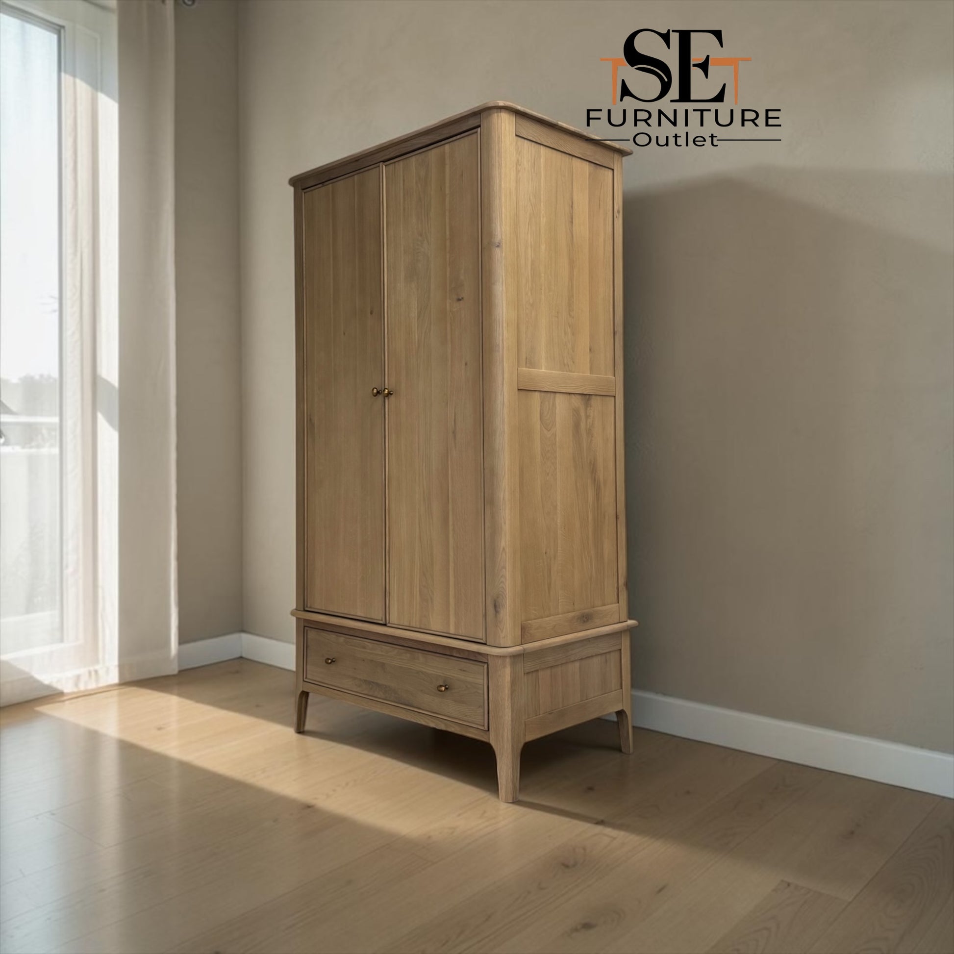 A tall light oak wood double-door wardrobe with a single drawer base, shown in a styled room corner with beige walls, light wood flooring, and a window on the left. The SE Furniture Outlet logo is visible in the top right corner.

