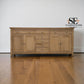 Wooden sideboard with multiple drawers and doors on a wooden floor, featuring the logo of SE Furniture Outlet.

