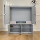 A large gray metal storage cabinet with its doors open, showing an organized interior with shelves and storage compartments. The cabinet is set against a beige paneled wall and light wood floor.

