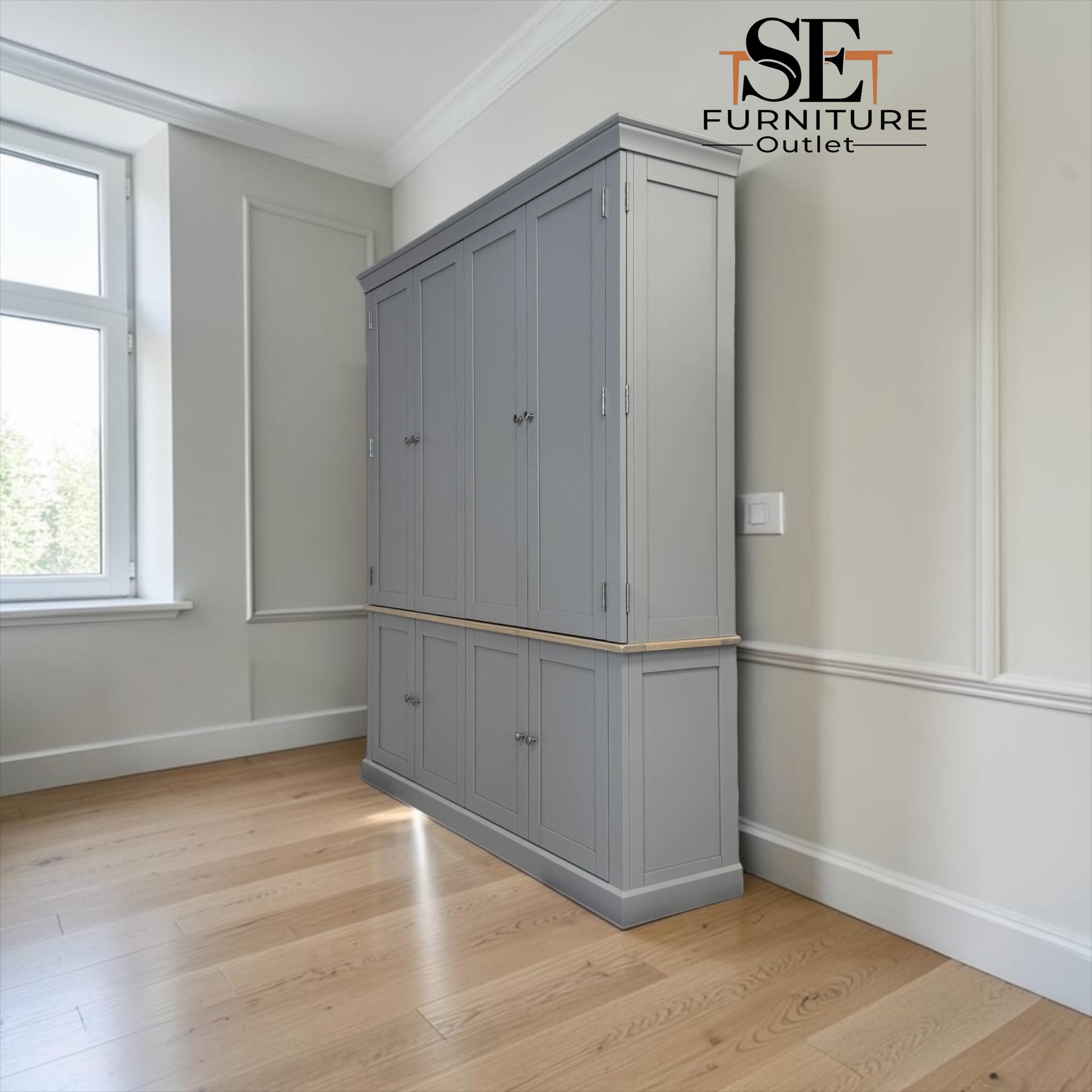 A tall gray wooden wardrobe or cabinet with multiple doors and drawers, shown in a bright room with light wood floors and cream walls. The SE Furniture Outlet logo is visible in the top right corner.

