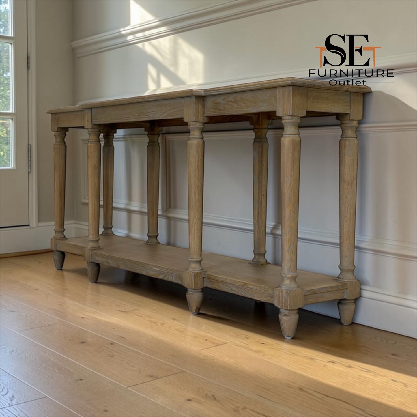 A light natural wood console table with turned legs and a lower shelf, shown in a room with hardwood floors and white paneled walls. The 'SE Furniture Outlet' logo is visible in the top right corner.

