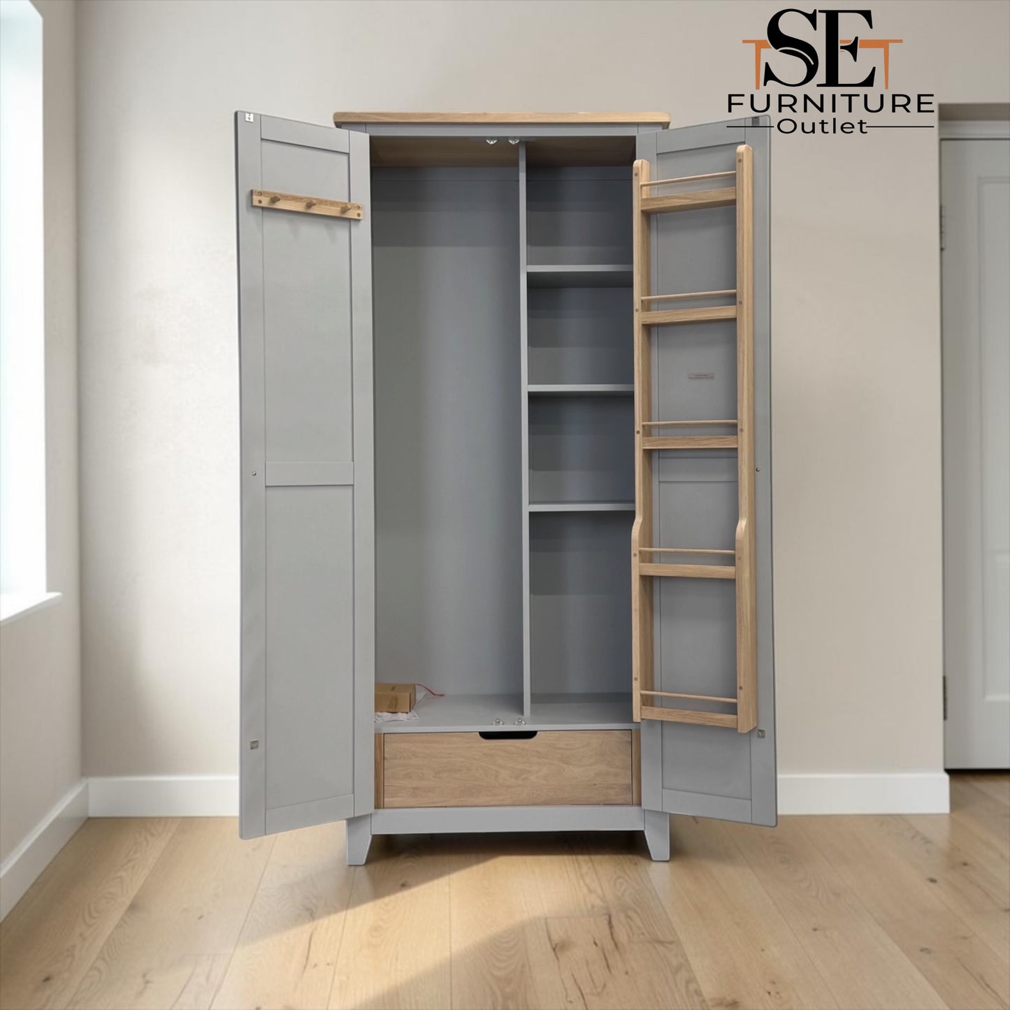 A tall gray wardrobe with open doors, showing light wood interior shelves, a hanging rod, and a drawer at the bottom, photographed in a room with light wood flooring. A 'SE Furniture Outlet' logo appears in the top right.


