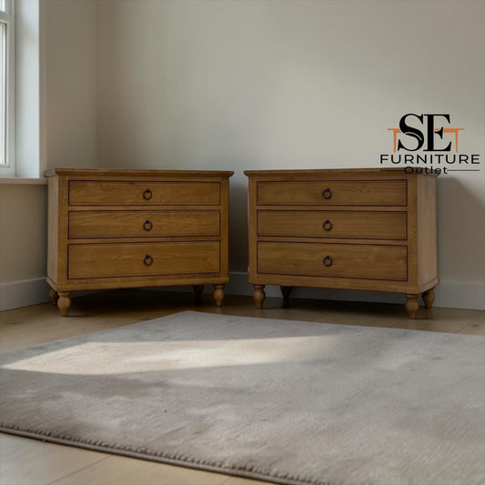 Two matching wooden three-drawer nightstands in a warm medium oak finish, positioned on a light-colored floor against a neutral wall with a gray rug in the foreground. The SE Furniture Outlet logo is visible in the top right corner.

