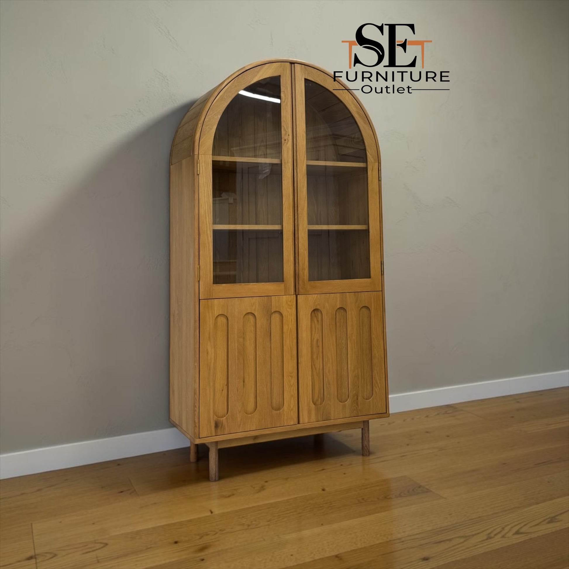 An arched wooden display cabinet with glass-paneled upper doors and paneled lower doors, shown in a room with a beige wall and wood floor. The SE Furniture Outlet logo is visible in the top right corner.

