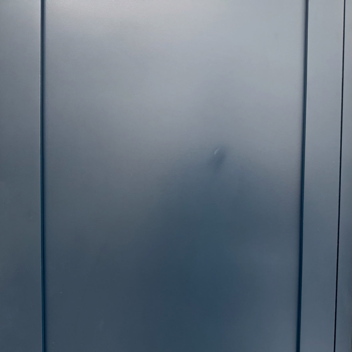 A close-up of a matte dark gray or slate-blue door panel with vertical seam lines.

